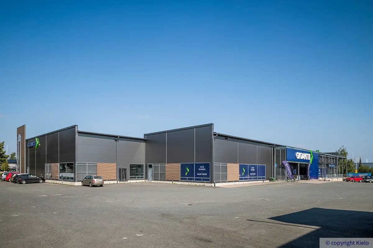 Tiiriön Big Box 2 tummanharmaa julkisivu pihan puolelta. Rakennuksen julkisivussa on puurima-aksentteja ja valomainokset.