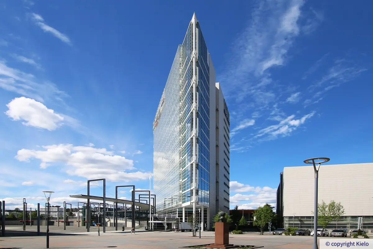 Kolmion muotoisen Innova 1 -toimitilakiinteistö kuvattuna terävä kärki etualalla. Vieressä näkyy rautatien yli Jyväskylän matkakeskukseen johtava silta. Taustalla taivaalla ajelehtivia pilviä.