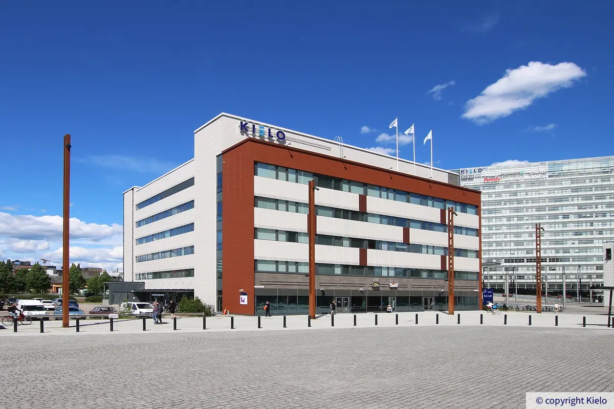 Innova 2, Lutakonaukio 7, Jyväskylä. Toimitilakiinteistön julkisivu on vaalea ja ruskea. Rakennuksen edessä kävelee ihmisiä kävelykadulla. Takana näkyy toinen Kielon rakennus