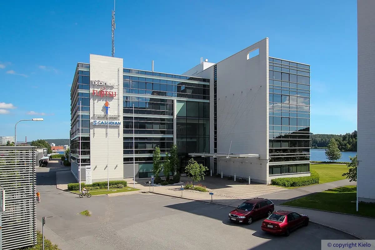 Jyväskylän Mattilanniemi 6-8, ulkokuva talon pääsisäänkäynnin kohdalta. Julkisivu on lasia ja valkeita elementtejä. Talon seinässä vuoralaisten valomainoksia.