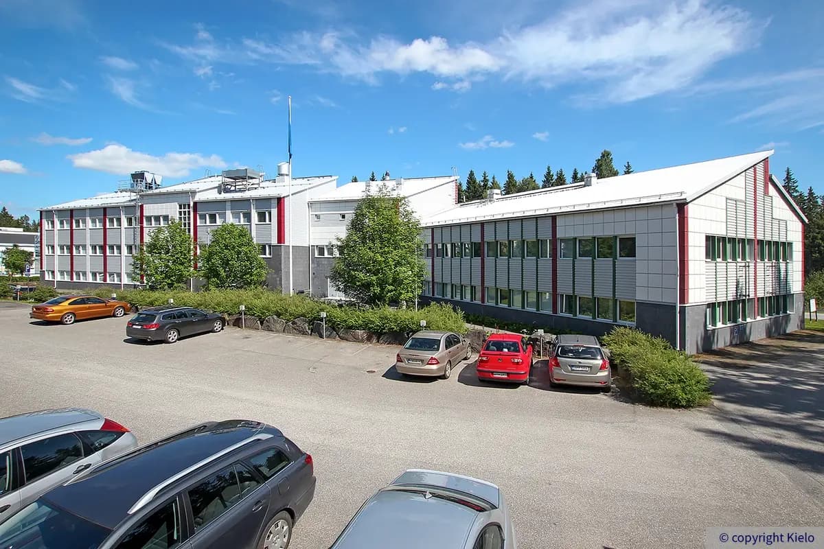 Jyväskylän Ylistönmäentie 31 kuvattuna sisäpihanpuolelta. Toimitilakiinteistö, joka on 2-3 kerroksinen. Talossa on viistokatto. Pihalla pysäköityjä autoja.