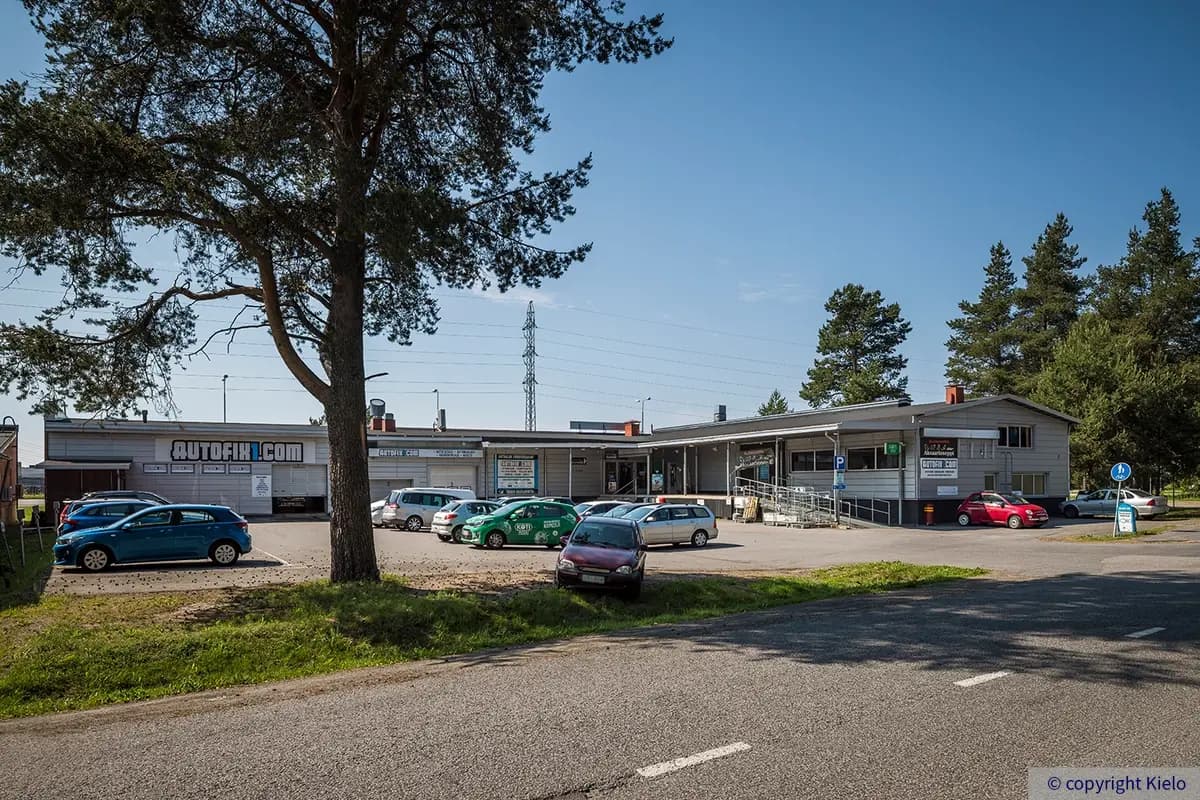 Toimitilarakennus Vuodintie 2 Oulu on L-n muotoinen. Talossa on harjakatto ja nosto-ovia. Talon edessä kasvaa iso mänty. Pihalla pysäköityjä autoja.