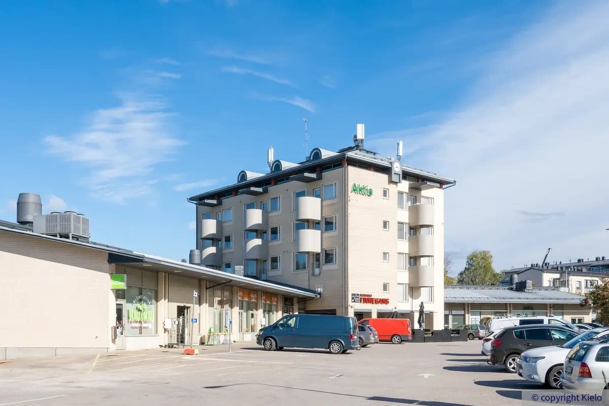 Tuusulan Hyrylänkatu 8, ulkokuva. Vaalea rakennus jonka edustalla autoja pysäköitynä, taustalla näkyy sininen taivas.