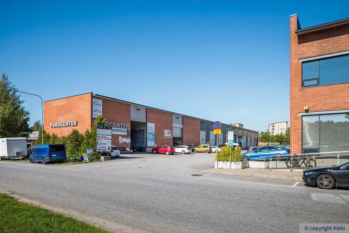 Purocenter pihan puoleinen punatiilinen varastorakennus. Nosto-ovellisien hallien edessä autoja, ensimmäisessä tilassa autopesula.