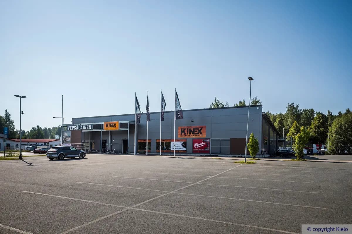 Tiiriön Big Box 1 tummanharmaa julkisivu pysäköintialueelta. Edessä on kiinteistössä toimivien liikkeiden kyltit ja liput.