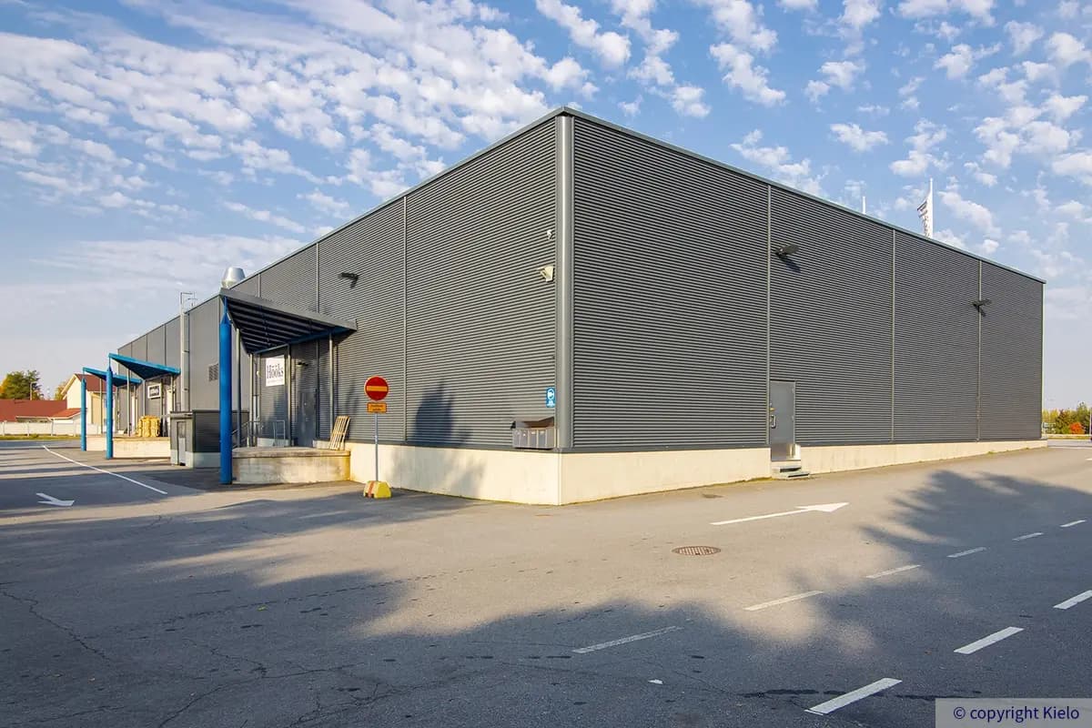 Seinäjoen Päivölänkatu 2 pienemmän rakennuksen pääty, jossa sivuovi. Takana lastausalueita.