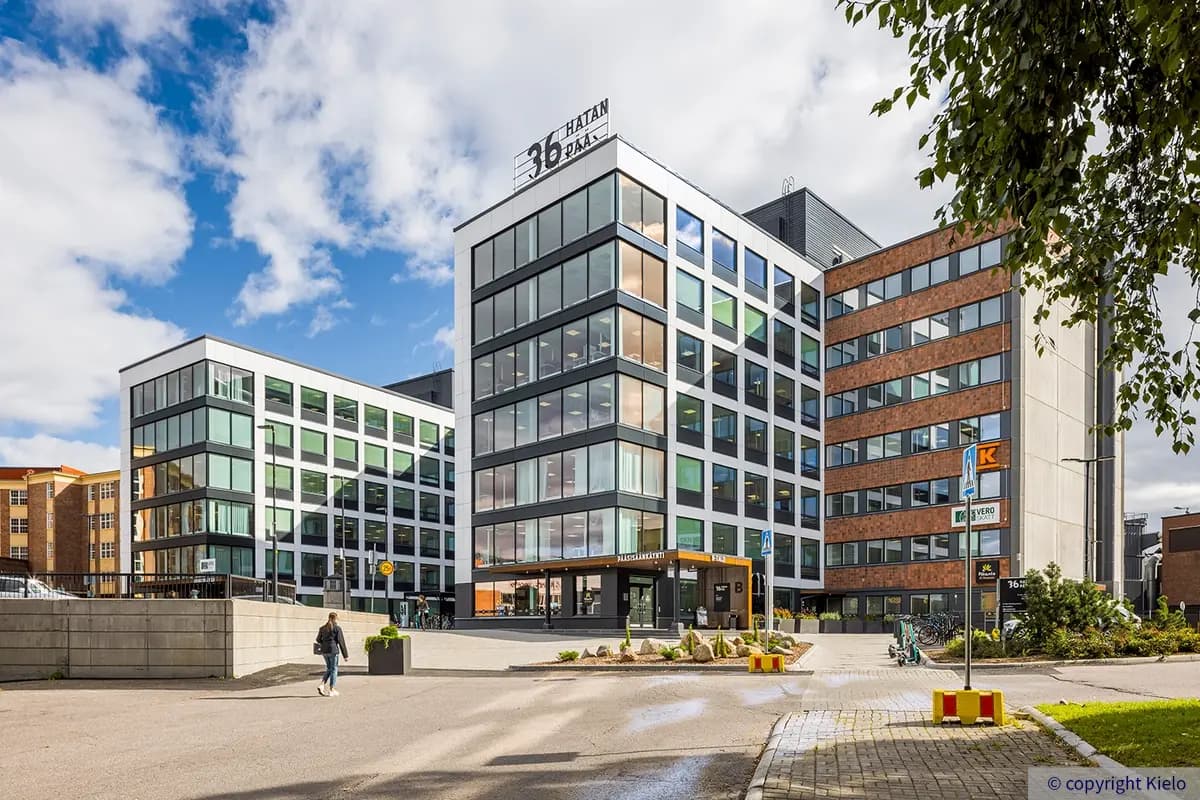 36Hatanpää julkisivu, jossa suuret ikkunat, oranssi katos pääsisäänkäynnin yllä ja kiinteistön logo valomainoksena katolla.