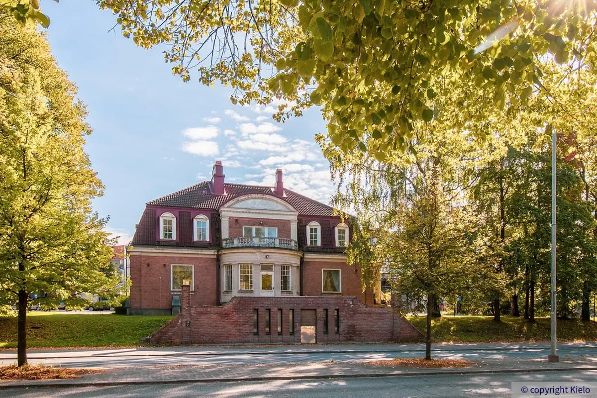 36Hatanpään Konsulitalon julkisivu kadulle. Talon päädyssä on parveke. Edessä pieni tiilimuuri, jossa ovi kellarikerrokseen.