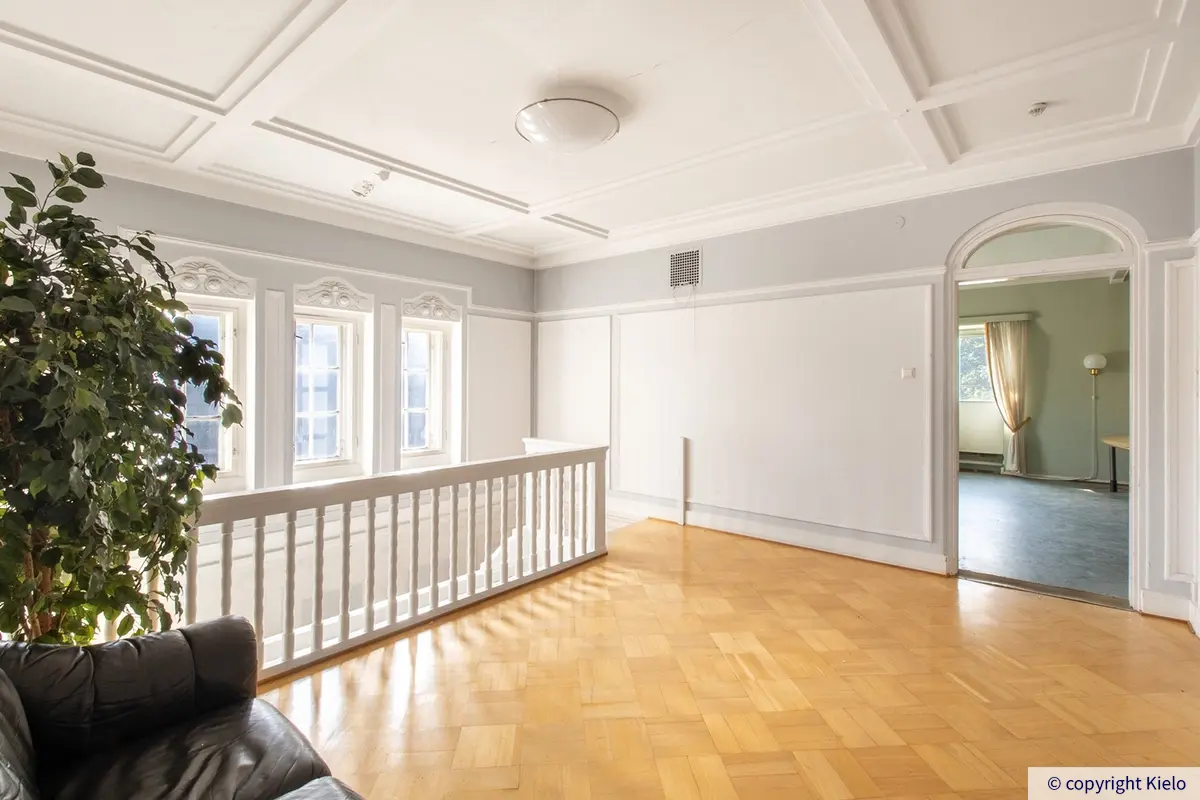 Konsulitalon toisen kerroksen huone portaiden yläpäässä. Vaaleassa tilassa on koristekuvioidut ikkunanpielet ja katto.