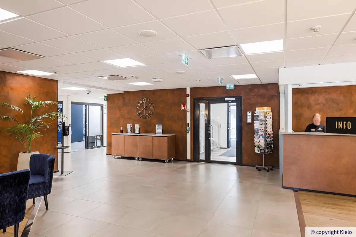 36Hatanpää aula. Ruskeaseinäisessä tilassa on infopiste/aulapalvelu ja odotustilaa.