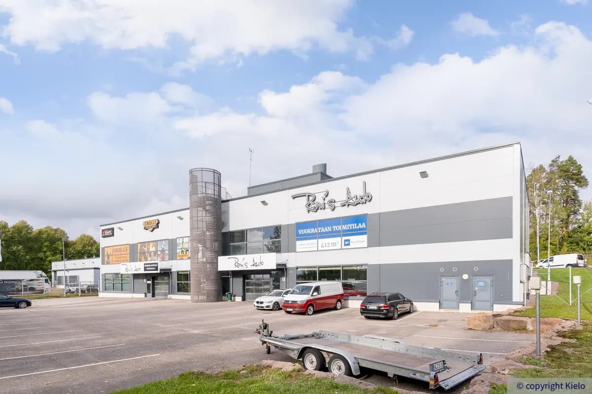 Espoon Kartanonherrantie 7, ulkokuva. Kaksikerroksinen vaaleanharmaa rakennus. Pihalla pysäköintialue jossa autoja pysäköitynä.