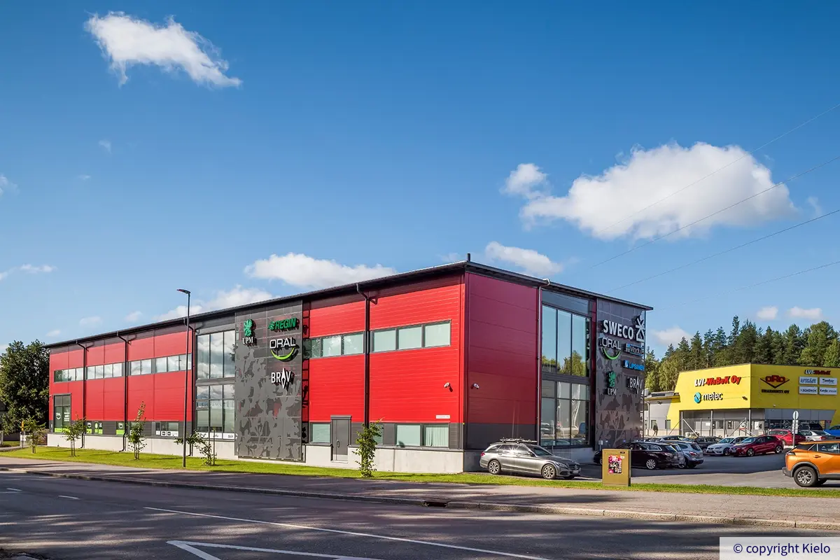 Jyväskylän Vasarakatu 23 A punainen julkisivu kadulta. Koristekuvioiduissa ritilöissä on asennettuna valomainoksia.