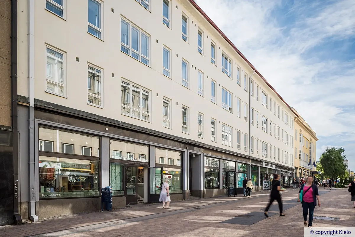 Jyväskylän Kauppakatu 18 vilkkaan kävelykadun varrella.  Katutason liiketiloissa on korkeat näyteikkunat.