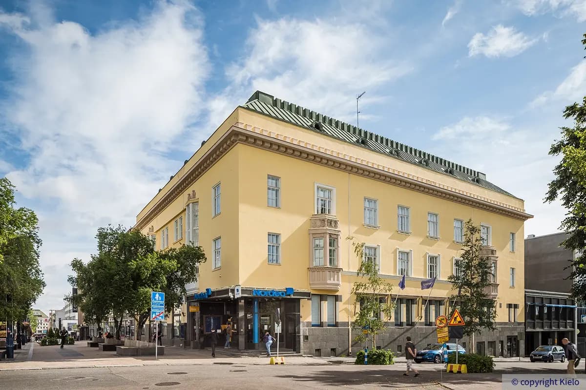 Keltainen toimitilakiinteistö Puistonkulman julkisivu. Katutasossa pankin konttori, vierestä alkaa kävelykatu.