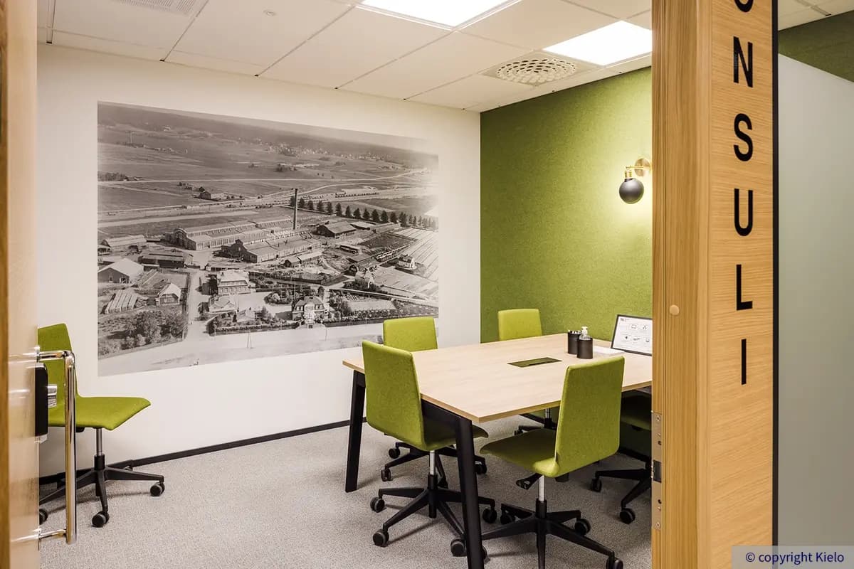 36Hatanpää pieni, viiden hengen neuvottelupöydällä varustettu kokoustila. Tilassa vihreä seinä ja tuolit, toisella seinällä vanha ilmakuva Lokomon halleista.