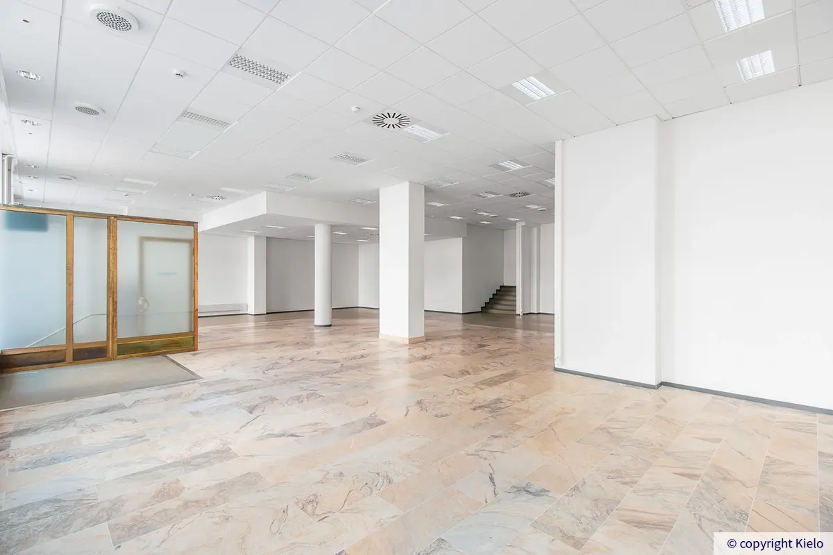 Puistonkulma valoisa marmorilattiainen ensimmäisen kerroksen liiketila. Avotilan takaosassa portaat toiseen osaan.