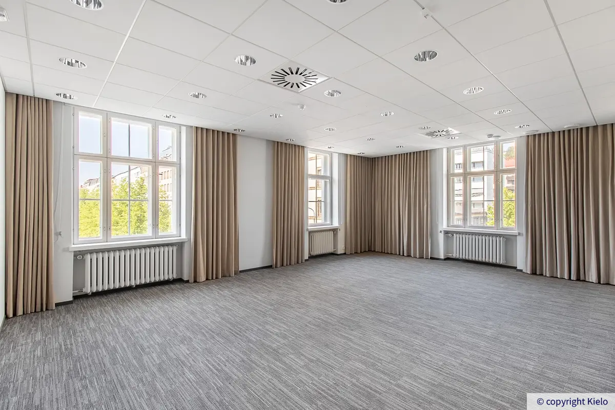 Puistonkulma avoin toimistotila, jossa kokolattiamatto ja ristikkoikkunat kahteen suuntaan.