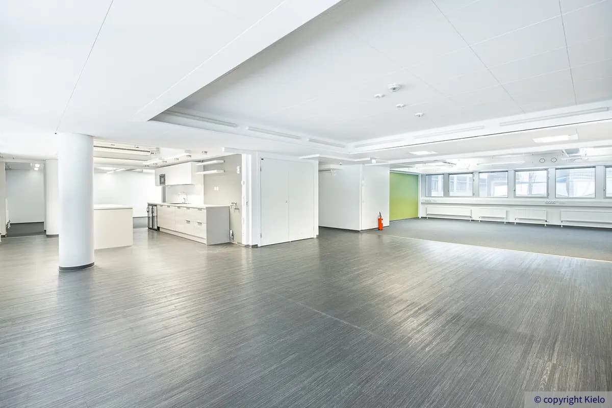 Jyväskylän Vapaudenkatu 48-50 avotoimisto, jossa laminaattilattiaa ja kokolattiamattoa. Kapeassa kohdassa keittiökalusteet.