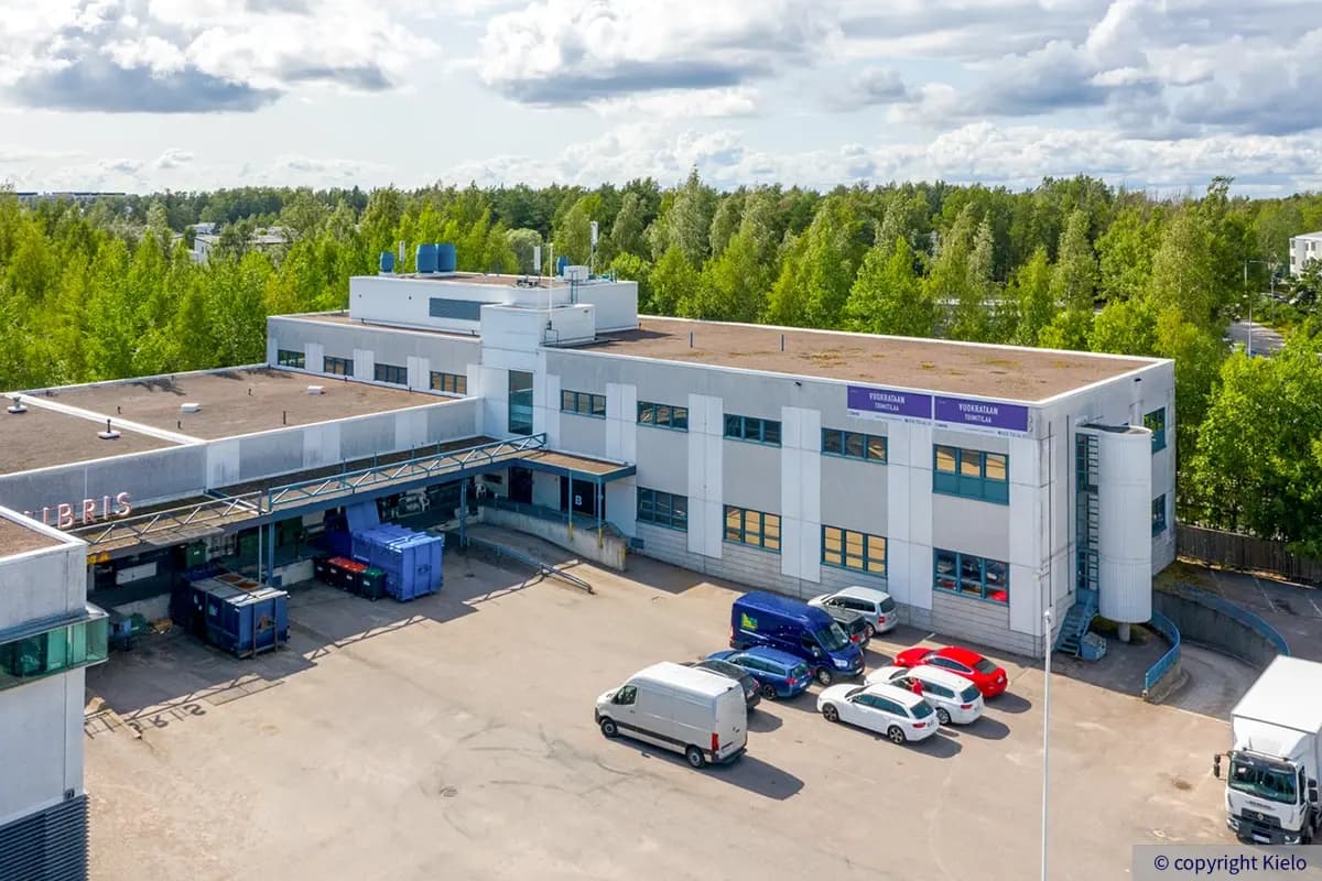 Helsingin Lirokuja 4 harmaa julkisivu. Sisäpihassa katoksen alla lastauslaituri, ja päädystä laskee ramppi pysäköintihalliin.