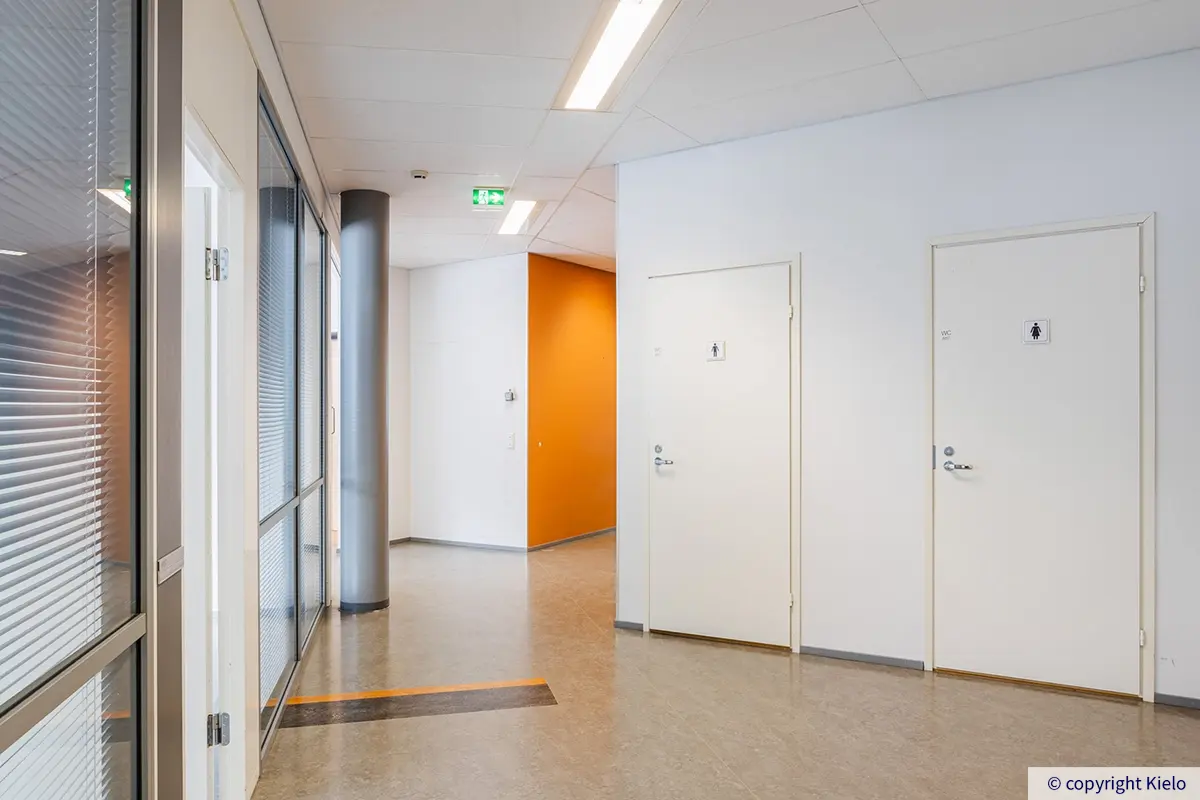 Jyväskylän Ohjelmakaari 10 ensimmäisen kerroksen 129 m² toimitilan käytävä, jossa lasiseinät toimistohuoneisiin ja ovet vessoihin.