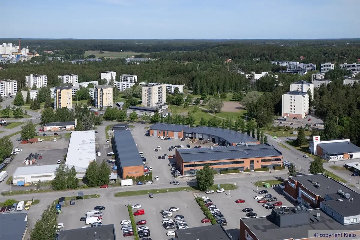 Purocenter punatiiltä ja harmaata peltiä yhdistävillä julkisivuilla olevat rakennukset, suurella sisäpihalla paljon autoja.