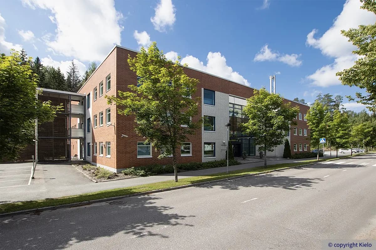 Kielo Lappeenranta – Teknologiapuistonkatu 10 toimitilakiinteistön punatiilinen julkisivu. Rakennuksen edessä vehreitä puita.