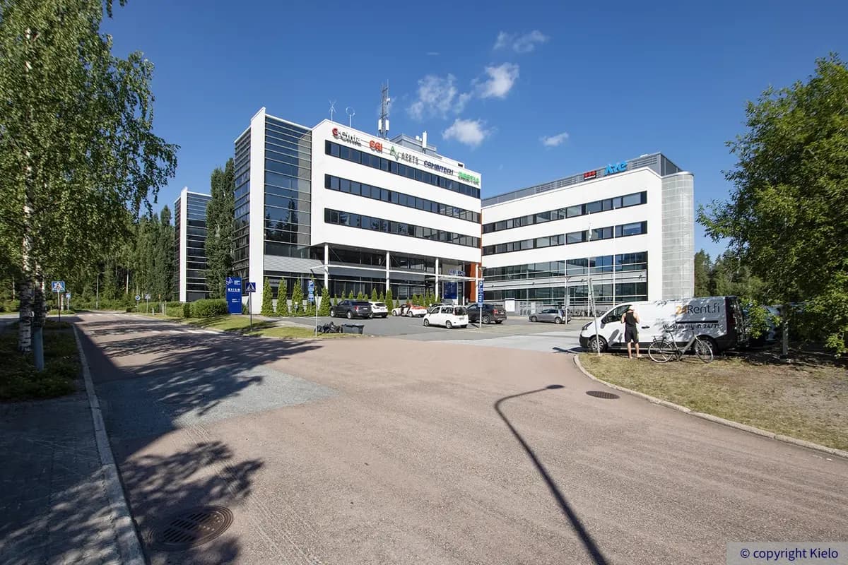 Jyväskylän Ohjelmakaari 2&10 toimitilakiinteistö, jossa yritysten logot rakennuksen yläreunassa. Edessä parkkipaikka, jossa autoja pysäköitynä.