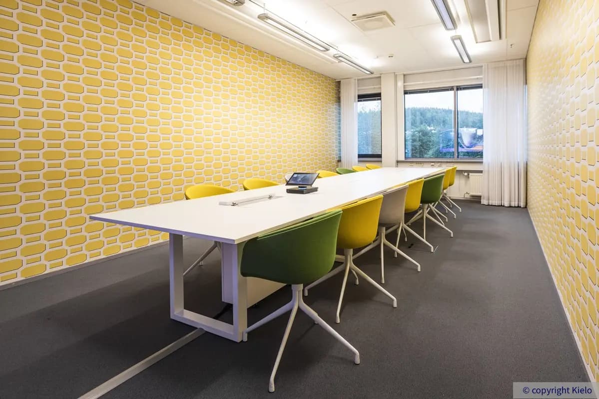 Jyväskylän Mattilanniemi 6-8 toimitilakiinteistön 1. kerroksen 1260 m2 toimitilan neuvotteluhuone, jossa keltaisella tapetilla tapetoidut seinät. Neukkarissa pitkä pöytä ja pöydän päässä ikkunat.
