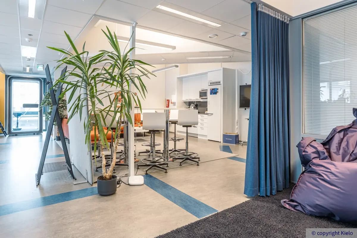 Innova 2 toimitilankiinteistön 3. kerroksen 131 m2 toimitilan keittiö, jossa valkoiset kalusteet. Tilassa oranssisohva ja korkea ruokapöytä, jonka ympärillä baarijakkaroita.