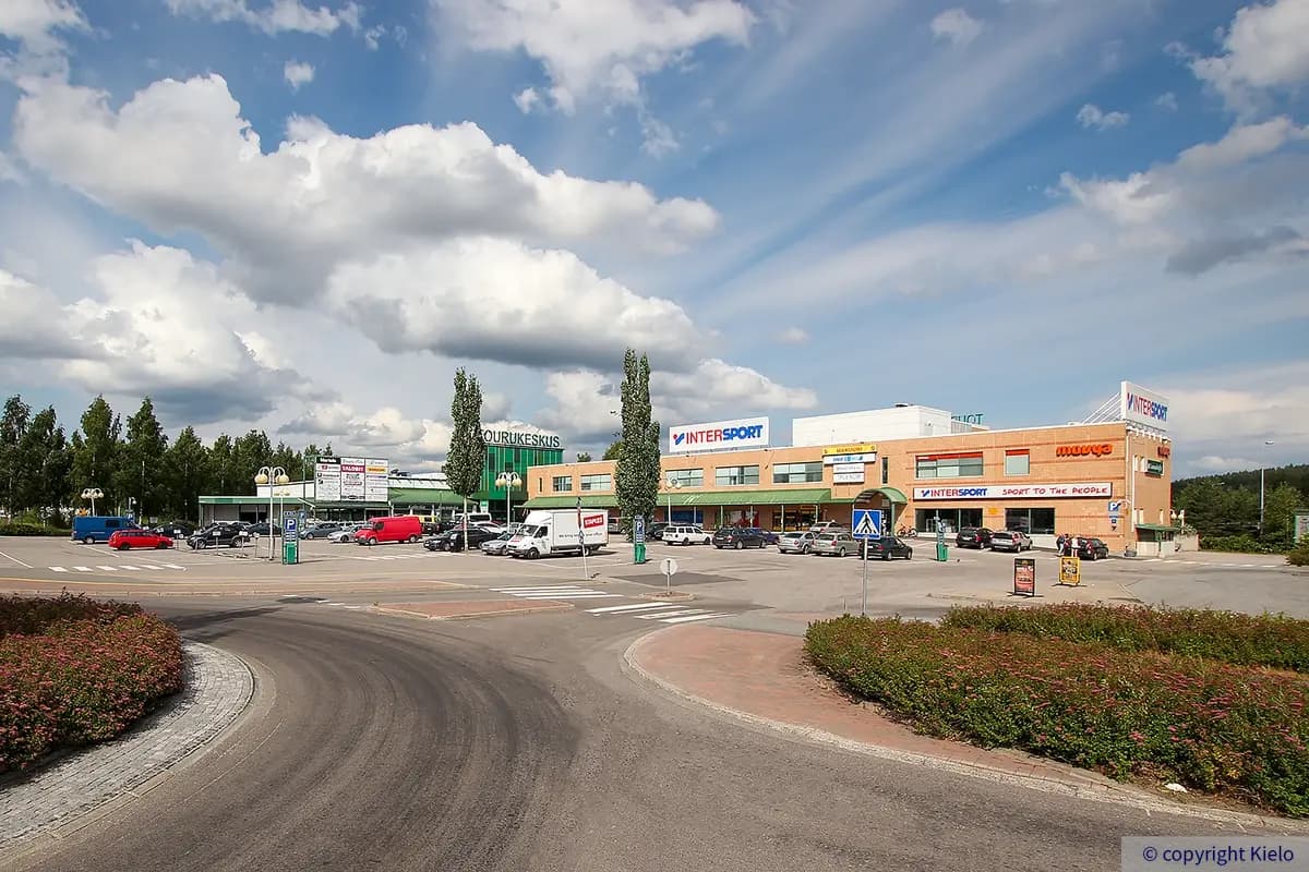 Liikekiinteistö Tourukeskus kuvattuna pihan sisäänajon kohdalta. Oikealla keltatiilinen siipirakennus, jossa vihertäviä toimitilojen ikkunoita. Talon edustalla on pysäköintialue, jolla autoja.