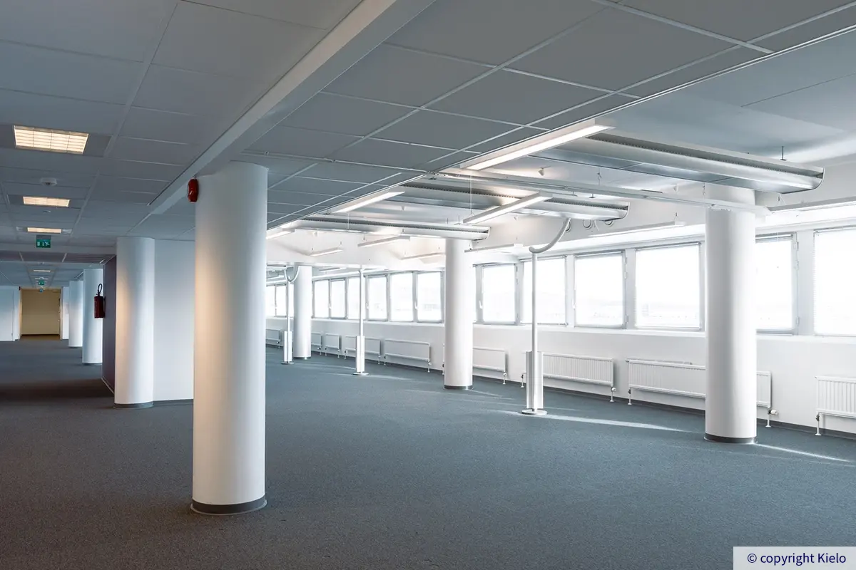 Jyväskylän Vapaudenkatu 48-50 osoitteessa sijaitsevan toimitilan avotila, jossa pitkä rivi ikkunoita ja useita pyöreitä pilareita. Lattiassa tumma kokolattiamatto.