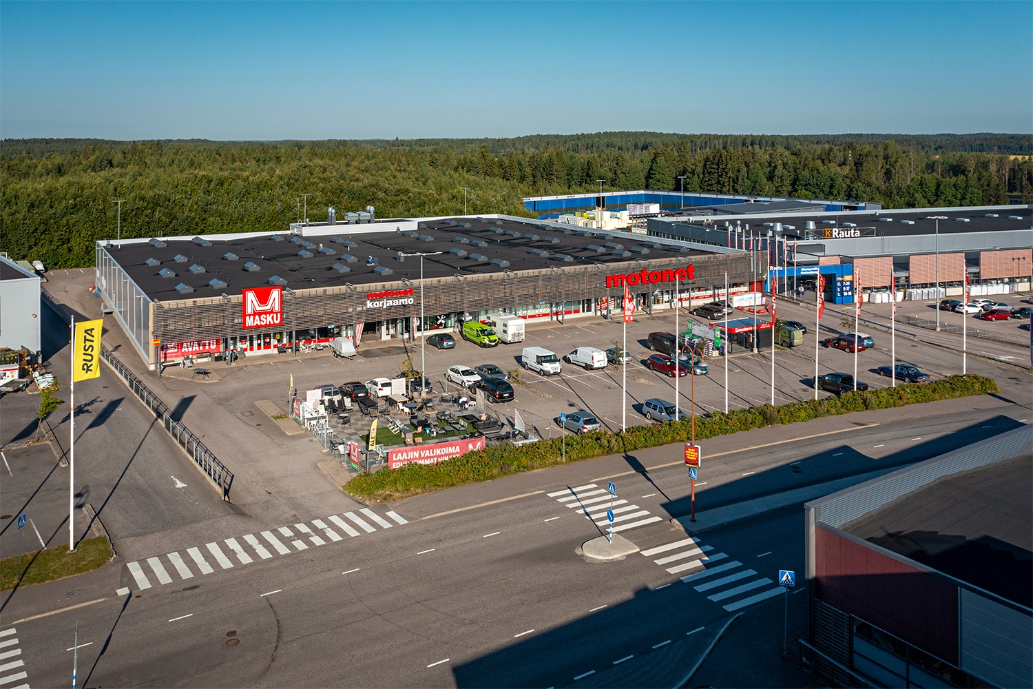 Suorakaiteen muotoinen, 1-kerroksinen liikekiinteistö Porvoon Ratsumestarinkatu 5-7 matalalta ilmasta kuvattuna. Liiketilojen edustalla on pysäköintialue, jolla useita henkilöautoja.