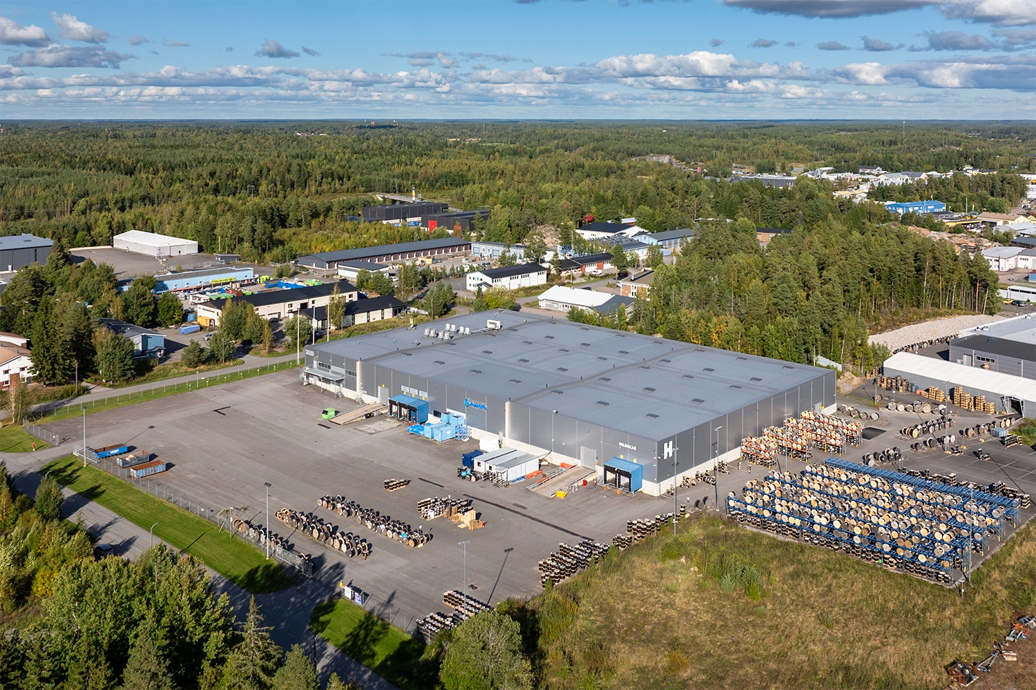 Kaarinan Asessorinkatu 3, ilmakuva. Kiinteistön julkisivu on harmaa, seinällä on neljä lastaustaskua ja kaksi ovea joista pääsee ajamaan autolla sisään. Edustalla paljon tilaa, taustalla metsikköä.