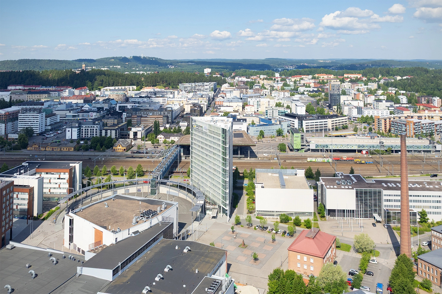 Ilmakuva 15 kerroksista, kolmion muotoisesta toimitilakiinteistöstä Innova 1. Valkea julkisivu, jossa on vuokralaisten valomainoksia. Vieressä Jyväskylän matkakeskus ja rautatieasema.